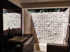 A bathroom with a stone wall, a sink, and a shower area. - Fabulous villa right on the beach with large pool, tropical garden & staff (Dencarik/Lovina)