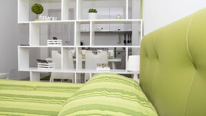 Een modern, wit interieur met een groene bank, een bed met een groen-geel gestreept sprei, en een witte kast met diverse objecten.