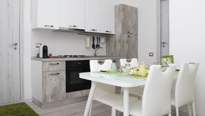 Een moderne keuken met witte kasten, een gasfornuis en een eethoek met een glazen tafel en witte stoelen.
