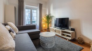 Una sala de estar moderna con un sofá gris, una mesa redonda de centro, un televisor de pantalla plana y una planta en maceta.