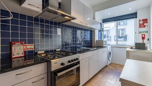 Una cocina moderna con estufa a gas, horno y lavadora, que presenta azulejos azules y muebles de cocina blancos.