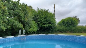 Piscina con escalera, rodeada de vegetación exuberante y un cielo nublado.