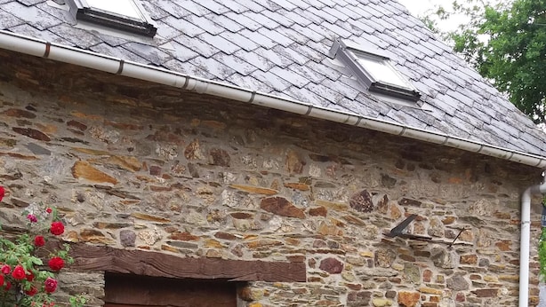 Un edificio de piedra con puerta y ventana de madera, una mesa con sillas y suelo de grava.