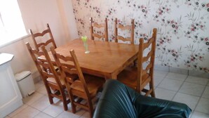 Un comedor con una mesa y sillas de madera, un cesto de basura pequeño y un papel tapiz con motivos florales.