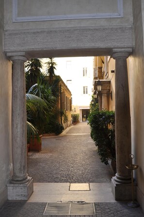A cobblestone alleyway framed by classical columns, leading to a building entrance.