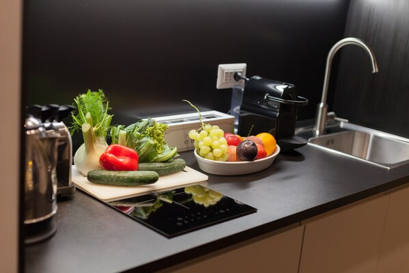 A kitchen counter with a cutting board, vegetables, a bowl of fruit, a toaster, and a sink.