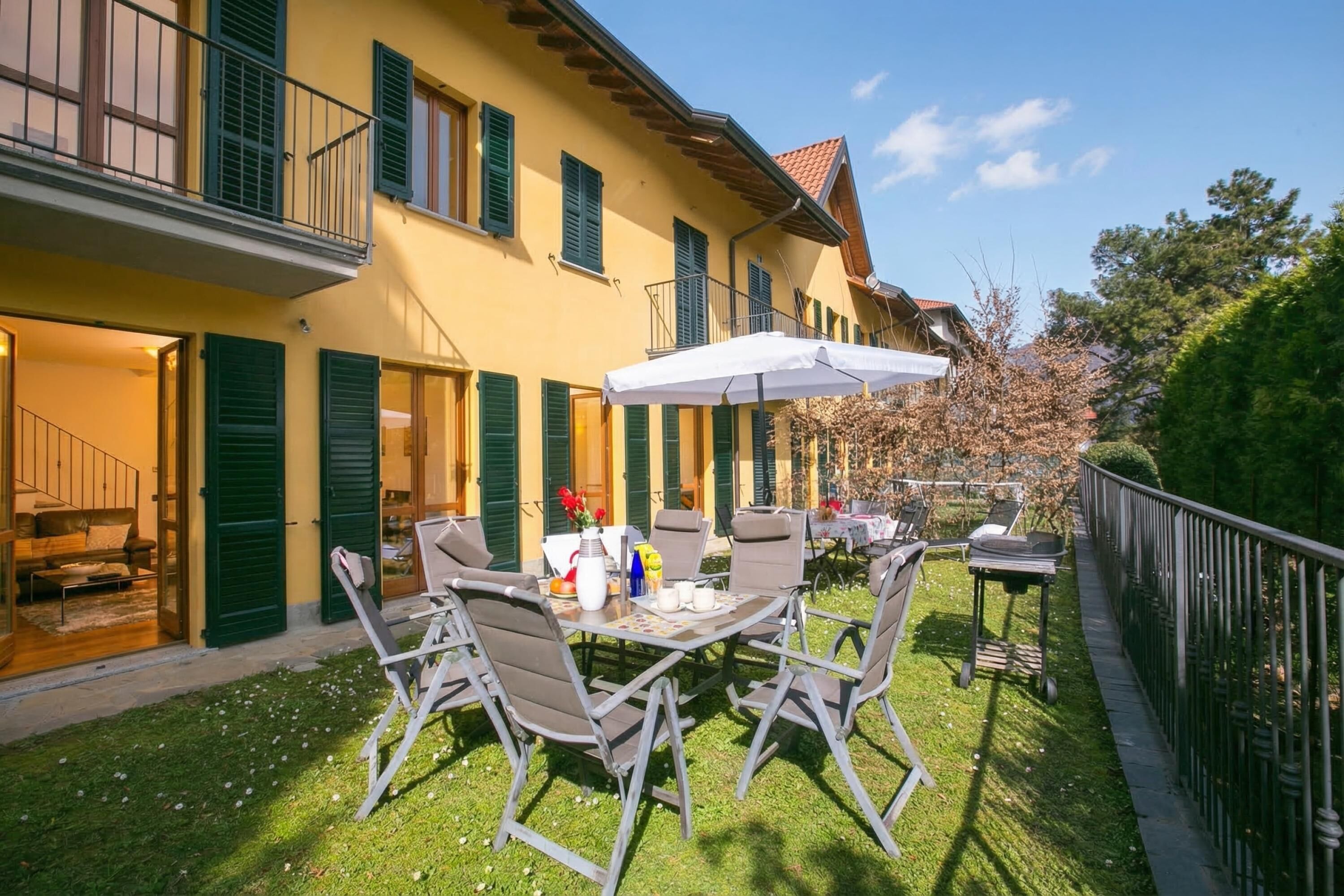 A patio with outdoor furniture, a table with a white umbrella, and a building with green shutters.