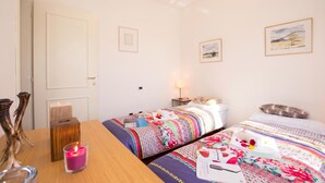Una habitación de hotel con dos camas, una mesa de madera, una vela y cuadros en las paredes.