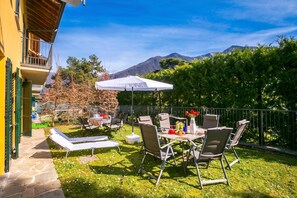 A patio with outdoor furniture, a table with a white umbrella, and a mountain view in the background. - Regina Villetta, Laglio, Italy (Laglio)