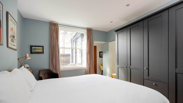 A bedroom with a large bed, a window with curtains, a desk, and a wardrobe.