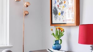 A modern room with a desk, a chair, a floor lamp, a vase with flowers, and a framed painting.