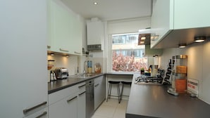 A modern kitchen with white cabinets, a stainless steel sink, a gas stove, and a window with autumn foliage.