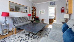 A living room with a grey sofa, a coffee table, a bookshelf, and a red lamp.