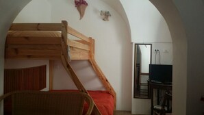 A bunk bed with a wooden frame, a red bedspread, a wicker chair, a small decorative item, and a television on a stand. - In Kasuzza. (Pantelleria) (Pantelleria)