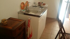 A compact kitchen with a sink, a stove, and a small table with a decorative bowl. - In Kasuzza. (Pantelleria) (Pantelleria)