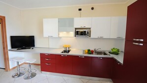 A modern kitchen with white and red cabinets, a built-in microwave, and a TV. - Residence Eden Magnolia 14, Argegno, Italy (Argegno)