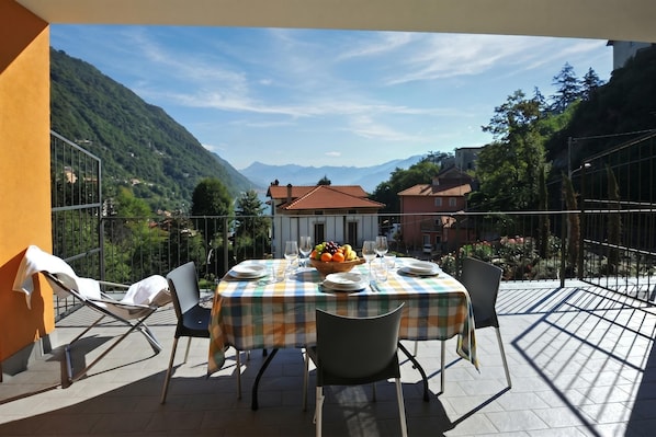 Una terraza con mesa lista para comer, sillas y un frutero.