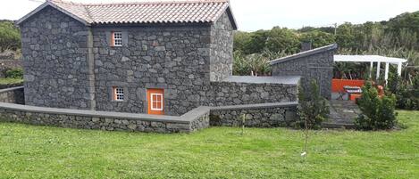 A stone house with a tiled roof, a small porch, and a grassy yard.