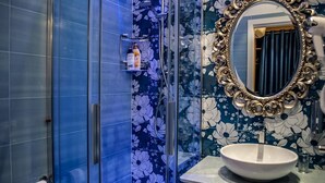 A bathroom with a glass shower enclosure, a white sink, and a decorative mirror with a floral tile backsplash. - Queen Suite (Vatican St. Peter's) (Roma)