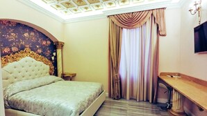 A bedroom with a tufted headboard, a bed with a patterned bedspread, a wooden bedside table, a nightstand, and a large window with curtains. - Queen Suite (Vatican St. Peter's) (Roma)