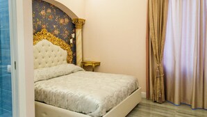 A bedroom with a large bed, a gold-framed headboard, a small bedside table, and a large window with curtains. - Queen Suite (Vatican St. Peter's) (Roma)