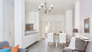 Ett modernt kök med vita skåp, en matplats med ett träbord och stolar samt en kristallkrona.