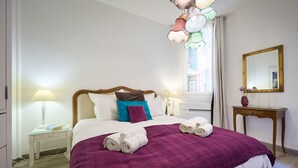 Ett hotellrum med en säng, ett nattduksbord med en lampa, ett litet träbord med en vas och en spegel på väggen.