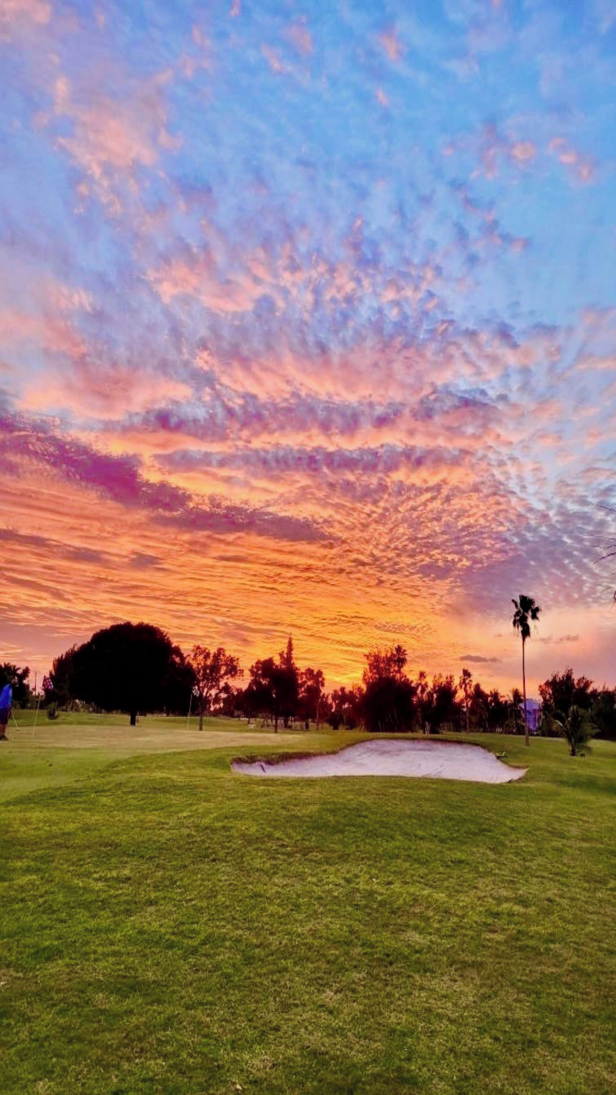 Un campo de golf con un búnker de arena y árboles al fondo durante el atardecer.