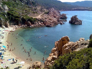 Une plage avec une eau cristalline, des rochers et des gens qui se baignent.