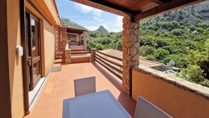 Ein Balkon mit weißem Tisch und Stühlen, einer Holz-Pergola und einer Stein-Säule.