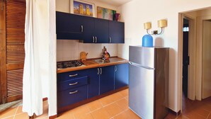 Eine kleine Küche mit dunkelblauen Schränken, einem Edelstahlkühlschrank und einem Fliesenboden.