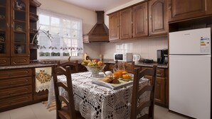 A kitchen with wooden cabinets, a white refrigerator, and a dining table set with fruits and pastries. - Viewpoint House (Ponta Sol)