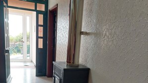 A hallway with a tiled floor, a black heater, a wall-mounted pipe, and a door with a green exit sign. - Viewpoint House (Ponta Sol)