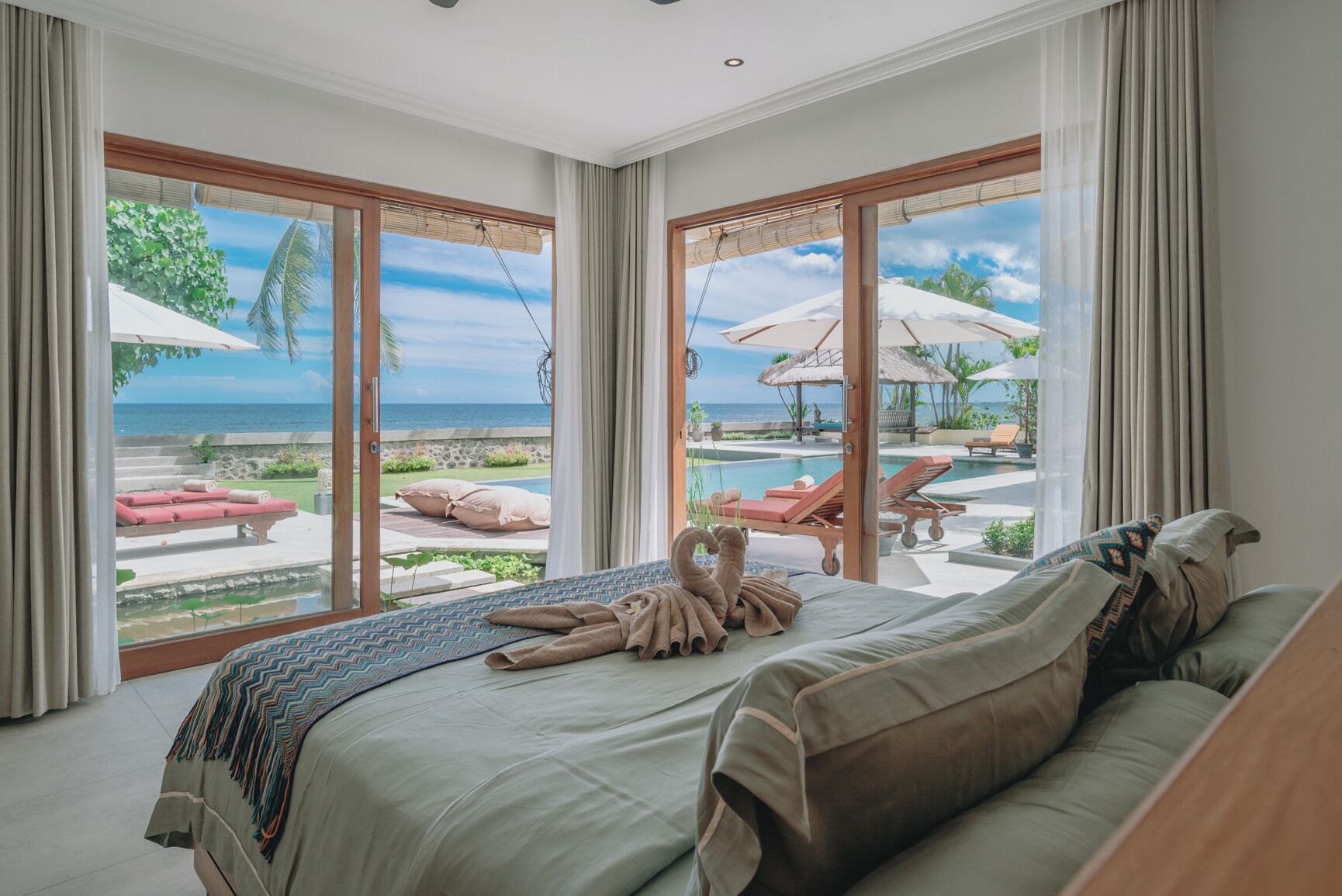 Une chambre dotée d’un grand lit, offrant une vue sur une piscine et des chaises longues, et située dans un cadre tropical en plein air.