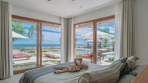Una camera da letto con un letto grande, vista su piscina e lettini, e un ambiente tropicale all'aperto.
