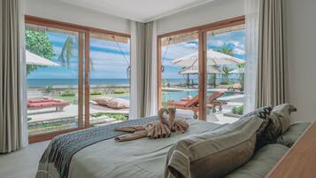 Une chambre dotée d’un grand lit, offrant une vue sur une piscine et des chaises longues, et située dans un cadre tropical en plein air.
