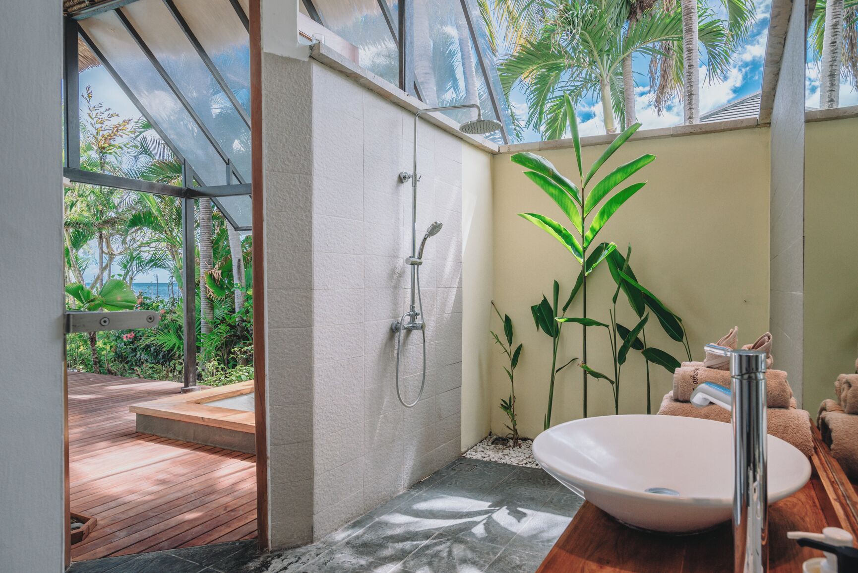 Une salle de bain dotée d’une grande fenêtre, d’une douche, d’un lavabo et d’une terrasse en bois à l’extérieur.