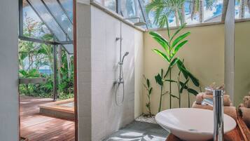 Une salle de bain dotée d’une grande fenêtre, d’une douche, d’un lavabo et d’une terrasse en bois à l’extérieur.