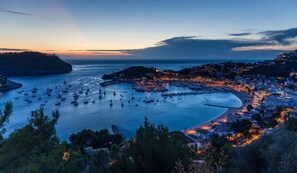 Un pueblo costero al atardecer con un puerto deportivo lleno de barcos, un faro y edificios a lo largo de la costa.
