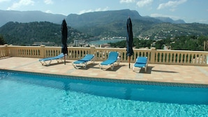 Area piscina con lettini e ombrelloni, affacciata su un paesaggio montuoso.