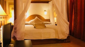 Un letto a baldacchino con lenzuola bianche e un drappo, un comodino, una lampada e un televisore.