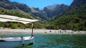 Una barca ormeggiata su una spiaggia con acqua cristallina, circondata da montagne e da una costa rocciosa.