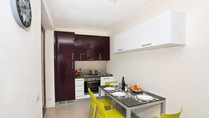 A compact kitchen with dark cabinets, a dining table set with yellow chairs, and a white ceiling light fixture. - Parco dei Cervi Terrazzo, Plesio, Italy (Plesio)