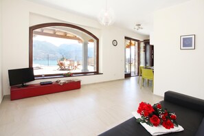 A living room with a TV, a red entertainment unit, a sofa, and a table with a bouquet of red roses. - Parco dei Cervi Terrazzo, Plesio, Italy (Plesio)