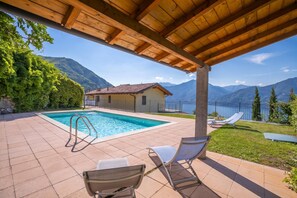 A pool area with a wooden pergola, two lounge chairs, and a view of mountains and a lake. - Parco dei Cervi Terrazzo, Plesio, Italy (Plesio)