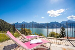 A balcony with two pink lounge chairs, a stone floor, and a view of a lake and mountains. - Parco dei Cervi Terrazzo, Plesio, Italy (Plesio)