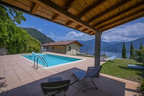 A pool with lounge chairs, a wooden pergola, and a mountain view.