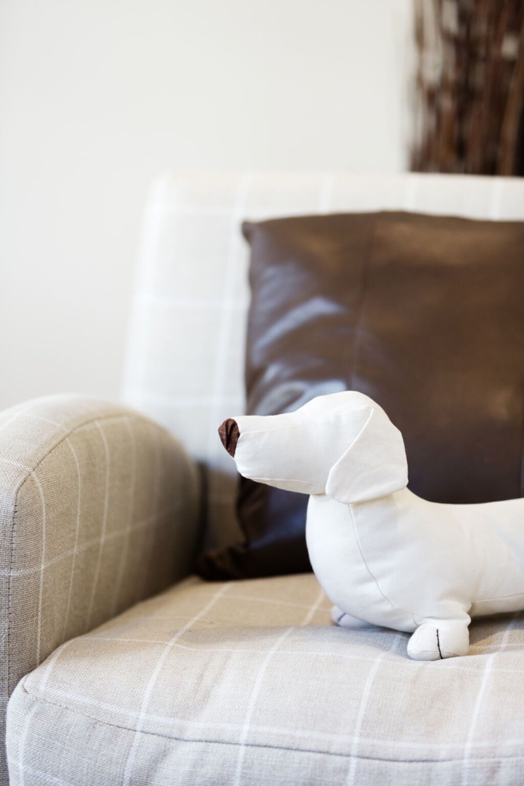A plush toy resembling a dog on a couch with a brown pillow in the background.