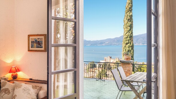 A balcony with a view of the sea and mountains, a table, chairs, a lamp, and a framed picture on the wall. - Villa Maria lake view, terrace, parking, garage, 7minutes walk to the village. (Verona)