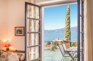 A balcony with a view of the sea and mountains, a table, chairs, a lamp, and a framed picture on the wall. - Villa Maria lake view, terrace, parking, garage, 7minutes walk to the village. (Verona)